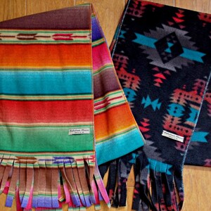 May include: Two colorful woven scarves with fringe. One scarf has a striped pattern in shades of red, orange, blue, and green. The other scarf has a geometric pattern in shades of black, gray, and blue. Both scarves have the text "Pathless Place" on the label.