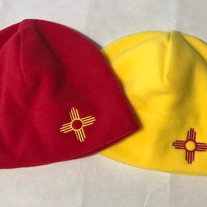 May include: Two fleece beanies with the New Mexico state symbol embroidered on them. One beanie is red and the other is yellow.