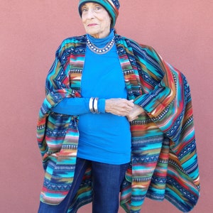 May include: A woman wearing a blue shirt, blue jeans, and a colorful patterned poncho. She is also wearing a colorful patterned hat.