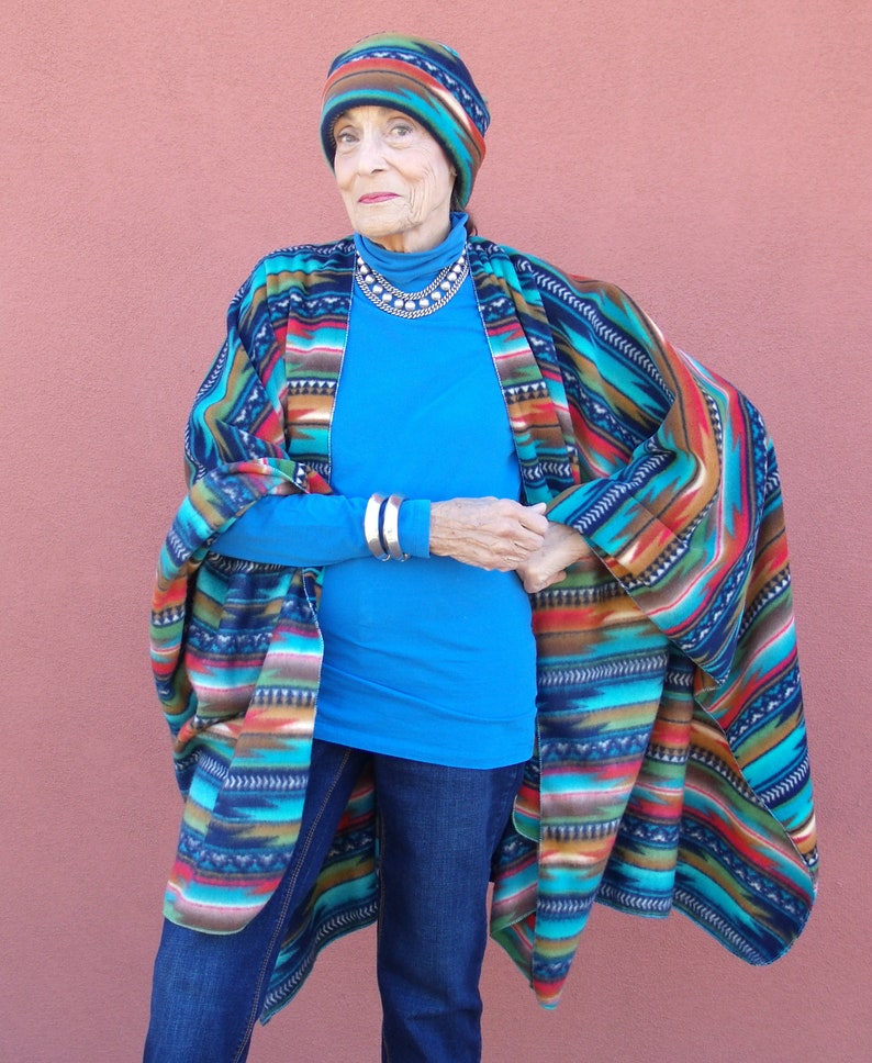 May include: A woman wearing a blue shirt, blue jeans, and a colorful patterned poncho. She is also wearing a colorful patterned hat.