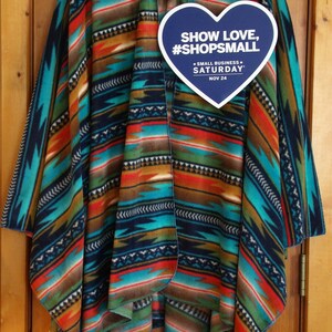 May include: A blue, red, green, and brown striped fleece poncho with a heart-shaped tag that says "Show Love, #ShopSmall - Small Business Saturday - Nov 24".