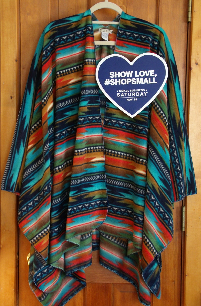 May include: A blue, red, green, and brown striped fleece poncho with a heart-shaped tag that says "Show Love, #ShopSmall - Small Business Saturday - Nov 24".