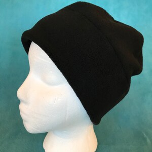 May include: A black fleece beanie hat on a white mannequin head. The hat is folded down at the top and has a seam running around the crown.