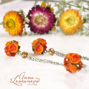 Peut inclure: Une paire de boucles d'oreilles en fleurs orange et rouge avec des cha&icirc;nes argent&eacute;es et des perles de cristal transparentes. Les boucles d'oreilles sont faites &agrave; la main et pr&eacute;sentent un motif floral d&eacute;licat.