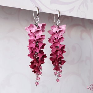 May include: Pink and red flower dangle earrings with crystal accents. The earrings are made of polymer clay and are a gradient of pink to red.