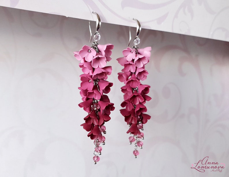 May include: Pink and red flower dangle earrings with crystal accents. The earrings are made of polymer clay and are a gradient of pink to red.