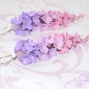 Peut inclure: Une paire de boucles d'oreilles pendantes avec un d&eacute;grad&eacute; de fleurs en p&acirc;te polym&egrave;re violettes et roses. Les boucles d'oreilles sont faites avec des crochets argent&eacute;s et ont une perle rose en haut.