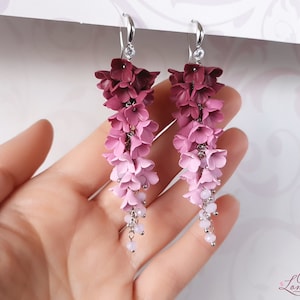 May include: A pair of dangle earrings with a gradient of pink and burgundy polymer clay flowers. The flowers are arranged in a cascading design and are accented with small silver beads.