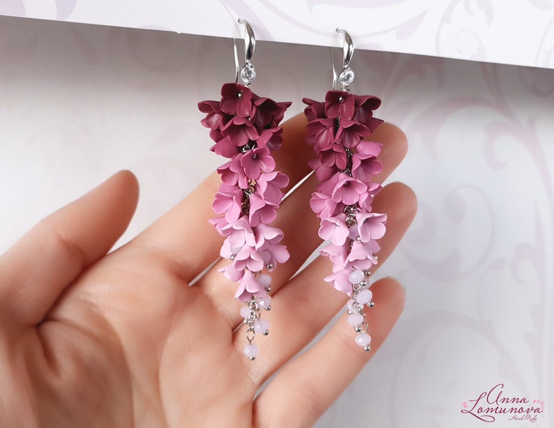 May include: A pair of dangle earrings with a gradient of pink and burgundy polymer clay flowers. The flowers are arranged in a cascading design and are accented with small silver beads.