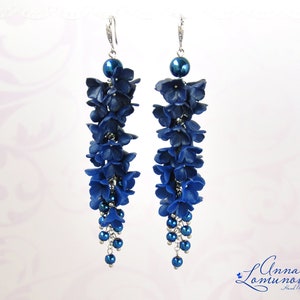 May include: A pair of long, dangling earrings featuring a cascade of dark blue flower-shaped beads. Each earring has a silver hook and a large, round blue bead at the top. The earrings are adorned with smaller blue beads at the bottom.