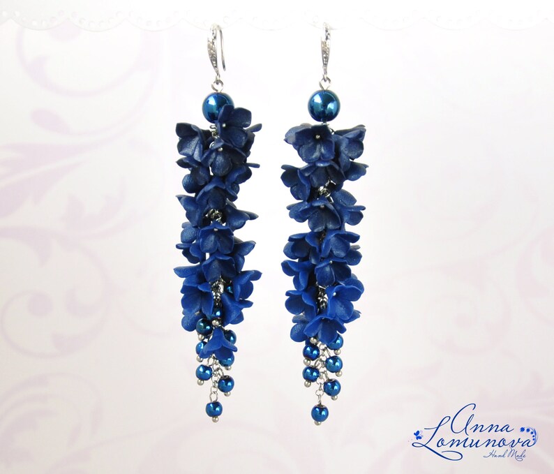 May include: A pair of long, dangling earrings featuring a cascade of dark blue flower-shaped beads. Each earring has a silver hook and a large, round blue bead at the top. The earrings are adorned with smaller blue beads at the bottom.