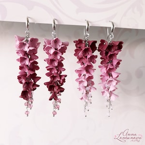 May include: A pair of dangle earrings with a gradient of pink and burgundy flowers. The earrings are made of polymer clay and have a silver hook.