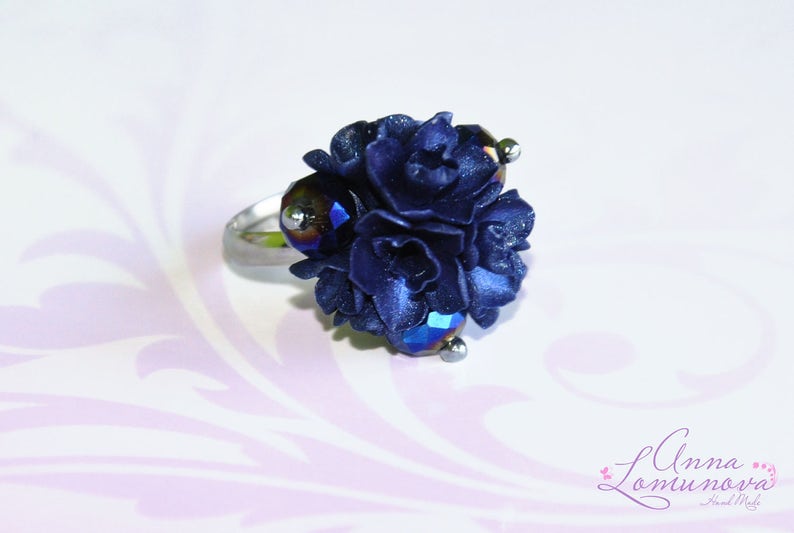 May include: A silver ring with a cluster of dark blue polymer clay flowers and iridescent glass beads.