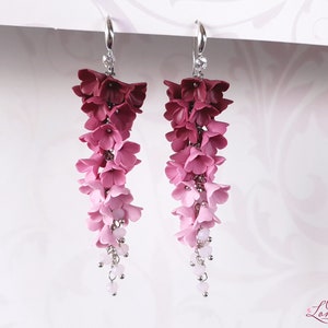 May include: A pair of long, dangling earrings with a gradient of pink and burgundy polymer clay flowers. The earrings are made with silver-toned metal and have small clear beads hanging from the bottom.