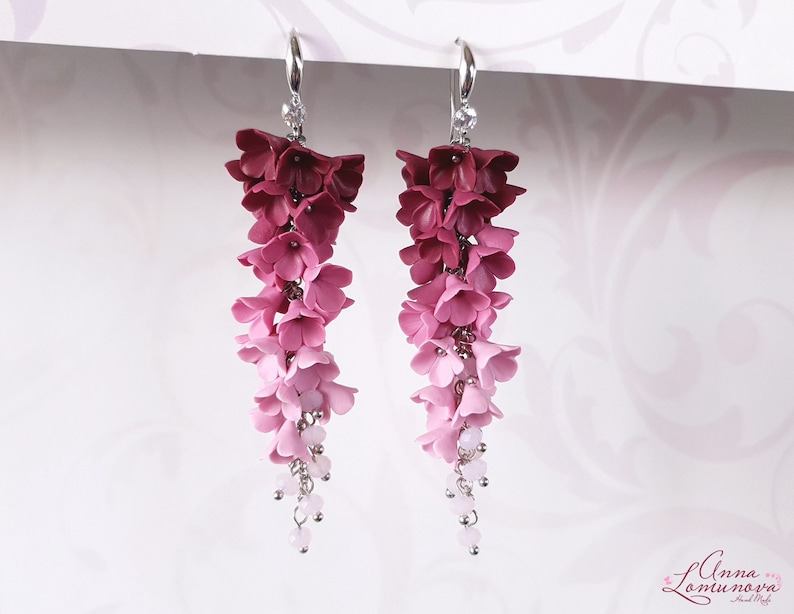 May include: A pair of long, dangling earrings with a gradient of pink and burgundy polymer clay flowers. The earrings are made with silver-toned metal and have small clear beads hanging from the bottom.