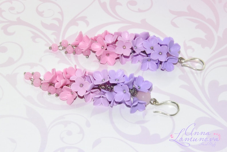 Peut inclure: Une paire de boucles d'oreilles pendantes avec un d&eacute;grad&eacute; de fleurs en p&acirc;te polym&egrave;re rose et violette. Les boucles d'oreilles sont faites avec des crochets en m&eacute;tal argent&eacute;.