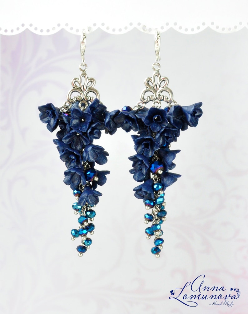 May include: A pair of dangle earrings with a cascade of dark blue polymer clay flowers and blue crystal beads hanging from silver filigree.