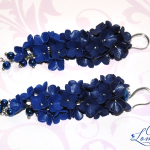 May include: A pair of dark blue floral earrings. Each earring features clusters of small, dark blue flowers with silver accents and dangling dark blue beads. The earrings have silver-colored ear wires.