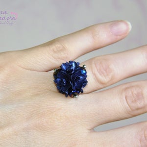 May include: A ring featuring a cluster of dark blue flowers, with a silver band.