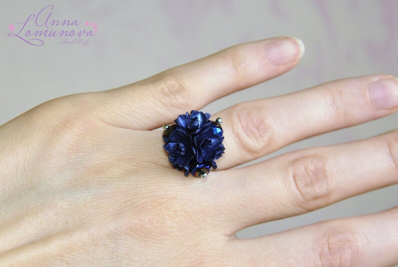 May include: A ring featuring a cluster of dark blue flowers, with a silver band.