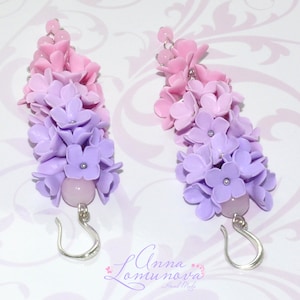 Peut inclure: Une paire de boucles d'oreilles longues et pendantes avec un d&eacute;grad&eacute; de fleurs en p&acirc;te polym&egrave;re rose et violette. Les boucles d'oreilles ont des crochets argent&eacute;s et une perle rose au bas.