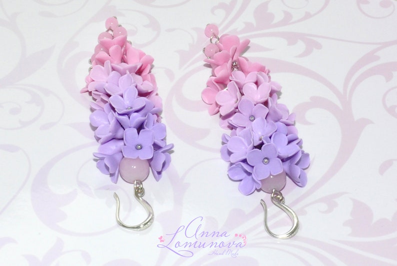 Peut inclure: Une paire de boucles d'oreilles longues et pendantes avec un d&eacute;grad&eacute; de fleurs en p&acirc;te polym&egrave;re rose et violette. Les boucles d'oreilles ont des crochets argent&eacute;s et une perle rose au bas.