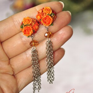 Peut inclure: Boucles d'oreilles en forme de fleurs orange et rouge avec des cha&icirc;nes argent&eacute;es et des perles de cristal transparentes.