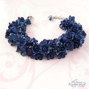 以下が含まれることがあります： ネイビーブルーの花のアクセントと虹色のビーズが特徴の手作りのブレスレット。 花柄のデザインは、シルバーカラーのチェーンと留め金にセットされています。 この繊細なジュエリーは、花のアクセサリーです。