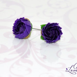 May include: A pair of purple flower stud earrings with green leaves. The earrings are made of polymer clay and are handmade.