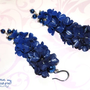 May include: A pair of handmade, dark blue floral earrings. Each earring features a cascade of small, textured flower petals and a cluster of dark blue beads. The earrings have silver-colored, curved ear wires.