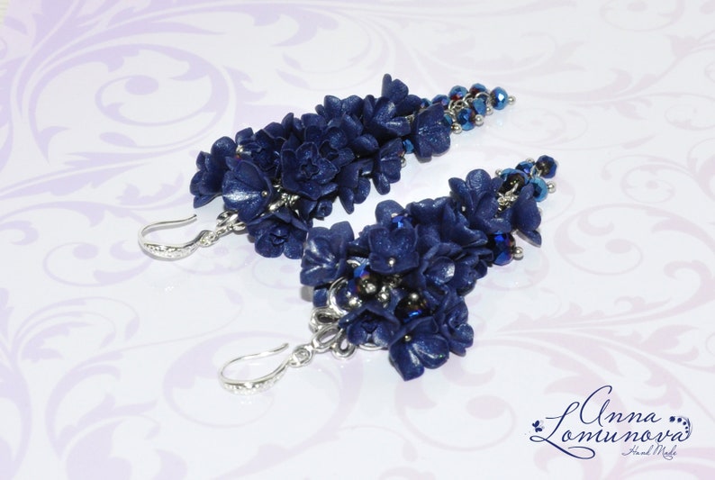 May include: A pair of dangle earrings featuring clusters of dark blue polymer clay flowers with silver accents and dark blue glass beads.