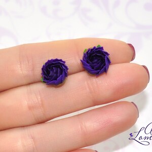 May include: A pair of purple flower stud earrings. The earrings are made of polymer clay and have a realistic flower design.