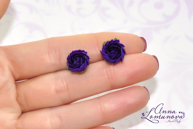 May include: A pair of purple flower stud earrings. The earrings are made of polymer clay and have a realistic flower design.