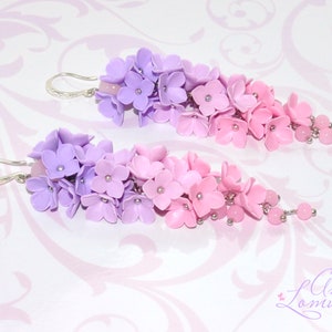 Peut inclure: Une paire de boucles d'oreilles pendantes avec un d&eacute;grad&eacute; de fleurs en p&acirc;te polym&egrave;re violettes et roses. Les boucles d'oreilles sont argent&eacute;es et ont une petite perle &agrave; l'extr&eacute;mit&eacute; de chaque pendentif.