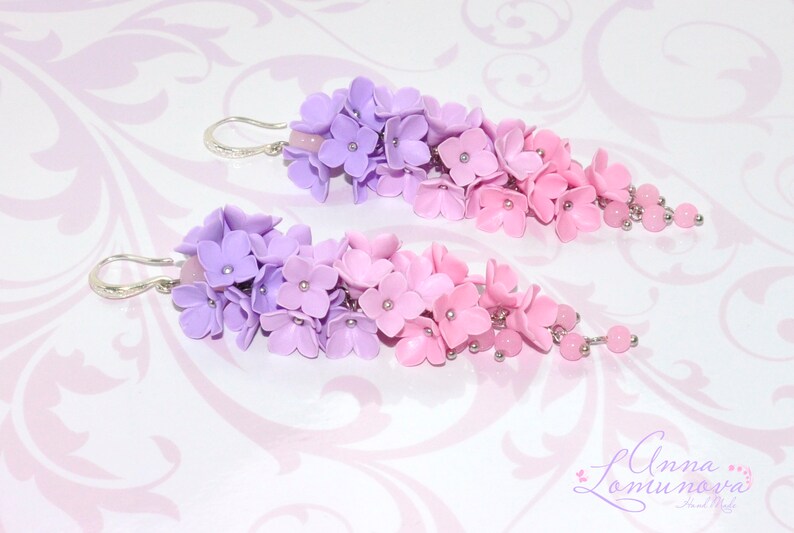 Peut inclure: Une paire de boucles d'oreilles pendantes avec un d&eacute;grad&eacute; de fleurs en p&acirc;te polym&egrave;re violettes et roses. Les boucles d'oreilles sont argent&eacute;es et ont une petite perle &agrave; l'extr&eacute;mit&eacute; de chaque pendentif.