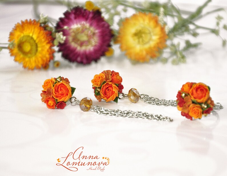 Peut inclure: Une paire de boucles d'oreilles en forme de fleurs orange et rouge avec des cha&icirc;nes argent&eacute;es. Les boucles d'oreilles sont en p&acirc;te polym&egrave;re et ont la forme de petits bouquets de fleurs.