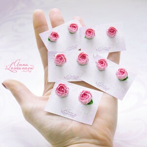Pode incluir: Um conjunto de oito brincos de flores cor-de-rosa em cart&otilde;es brancos. Os cart&otilde;es t&ecirc;m o texto "Anna Lamunova Hand Made" impresso neles.