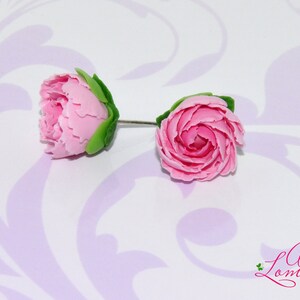 Pode incluir: Um par de brincos de argila polim&eacute;rica rosa em forma de rosas com folhas verdes. Os brincos est&atilde;o sobre um fundo branco com um padr&atilde;o floral roxo.