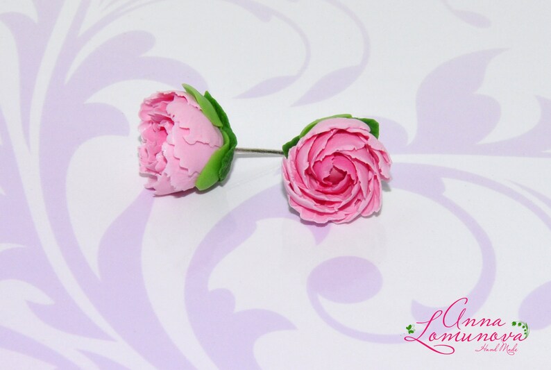 Pode incluir: Um par de brincos de argila polim&eacute;rica rosa em forma de rosas com folhas verdes. Os brincos est&atilde;o sobre um fundo branco com um padr&atilde;o floral roxo.
