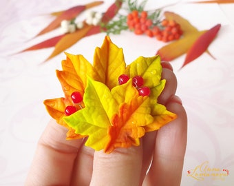 May include: A cluster of five fall leaves made of polymer clay, with shades of yellow, orange, and red. The leaves are arranged in a fan shape and have a few red berries attached to them.
