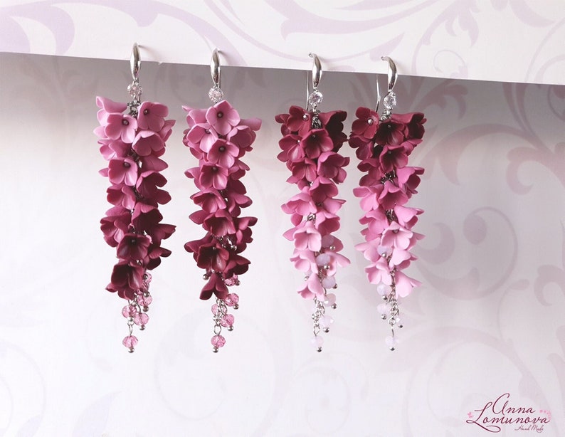 May include: A pair of long, dangling earrings with a gradient of pink and purple flowers. The earrings are made of polymer clay and have a silver finish.