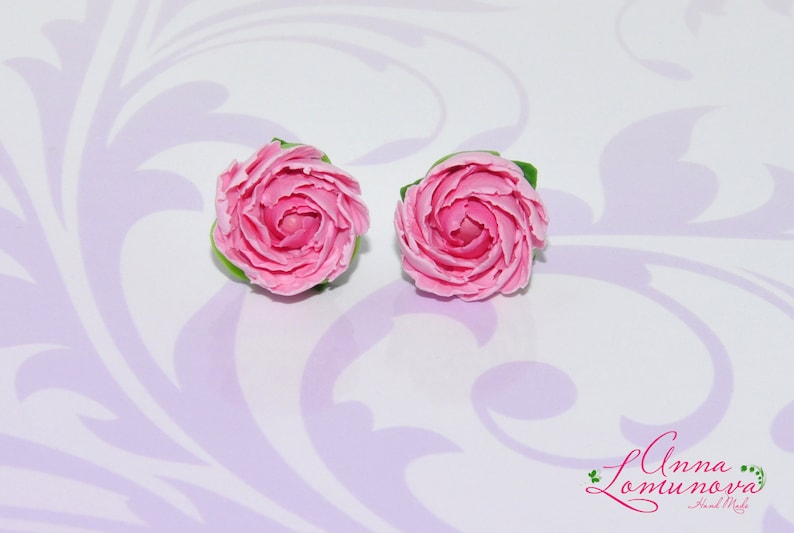 Pode incluir: Um par de brincos de argila polim&eacute;rica rosa em forma de rosas. Os brincos s&atilde;o feitos &agrave; m&atilde;o e t&ecirc;m um visual delicado e feminino.