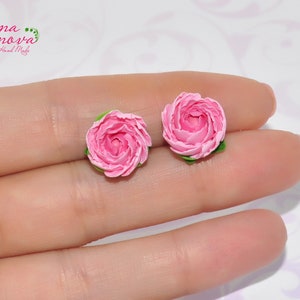 Pode incluir: Um par de brincos de argila polim&eacute;rica rosa em forma de rosas. Os brincos s&atilde;o pequenos e delicados, e seriam um presente encantador para um amigo ou ente querido.