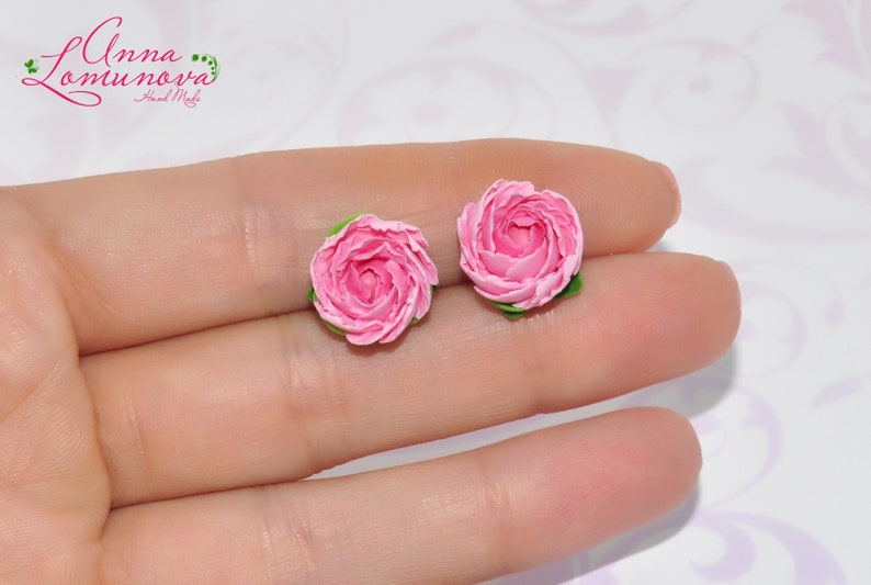 Pode incluir: Um par de brincos de argila polim&eacute;rica rosa em forma de rosas. Os brincos s&atilde;o pequenos e delicados, e seriam um presente encantador para um amigo ou ente querido.