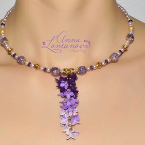 Peut inclure: Un collier de perles violettes et dor&eacute;es avec un pendentif de fleurs violettes en cascade. Le collier est compos&eacute; de petites perles rondes et a un accent dor&eacute;.