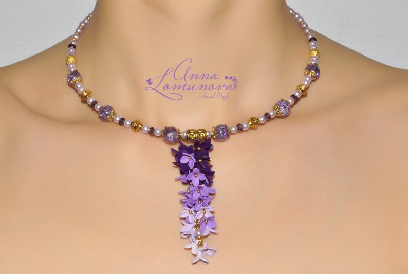 Peut inclure: Un collier de perles violettes et dor&eacute;es avec un pendentif de fleurs violettes en cascade. Le collier est compos&eacute; de petites perles rondes et a un accent dor&eacute;.
