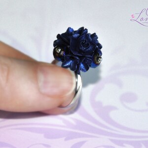 May include: A dark blue flower ring with silver accents. The ring is made of polymer clay and is a unique piece of jewelry.
