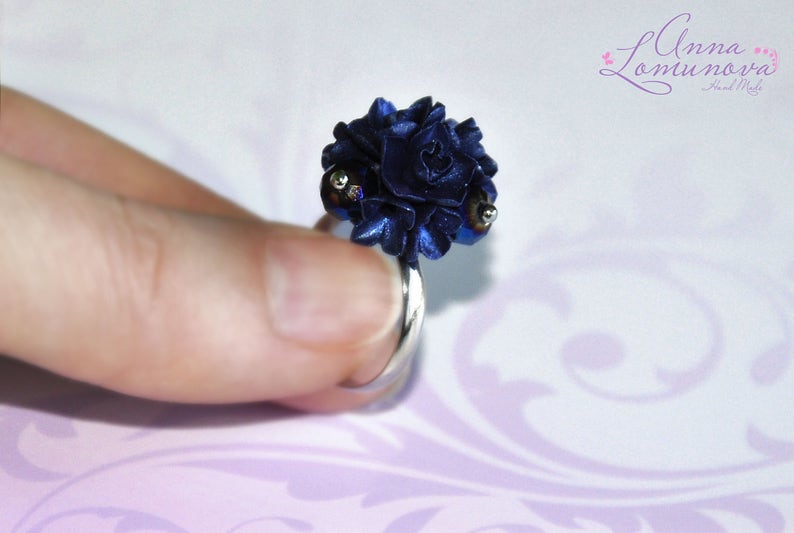May include: A dark blue flower ring with silver accents. The ring is made of polymer clay and is a unique piece of jewelry.