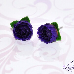 May include: A pair of purple polymer clay earrings shaped like roses with green leaves.