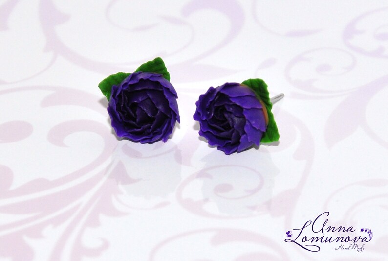 May include: A pair of purple polymer clay earrings shaped like roses with green leaves.